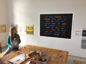 Kultur macht stark-Projekt 2019: Kind schaut auf Bild mit den Worten orange, blau, lila, grün, rot in 36-facher farbiger Ausführung
